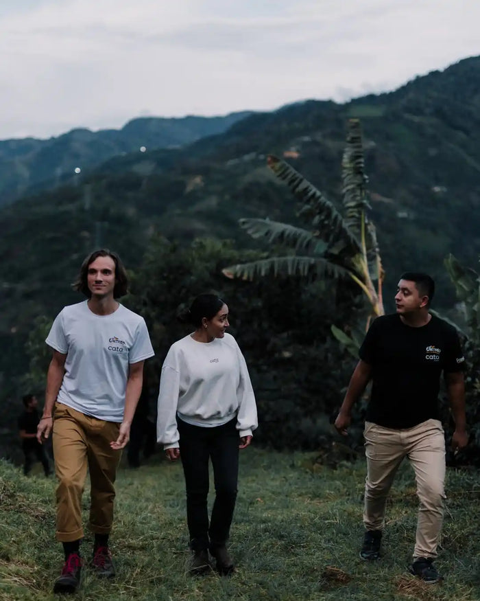 Three people walking in a scenic outdoor setting with mountains and greenery.