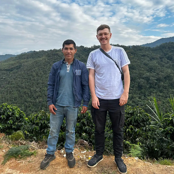 Two people standing on a mountain with a scenic view of green hills and blue sky.